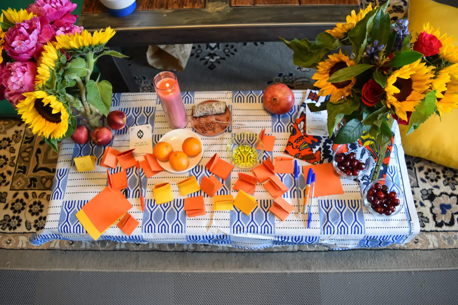 A shrine laid out on a patterned cloth with sunflowers, roses and folded cards.