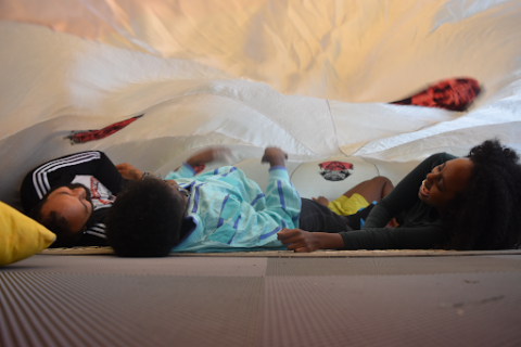 Three people lay under a tent, smiling and laughing.