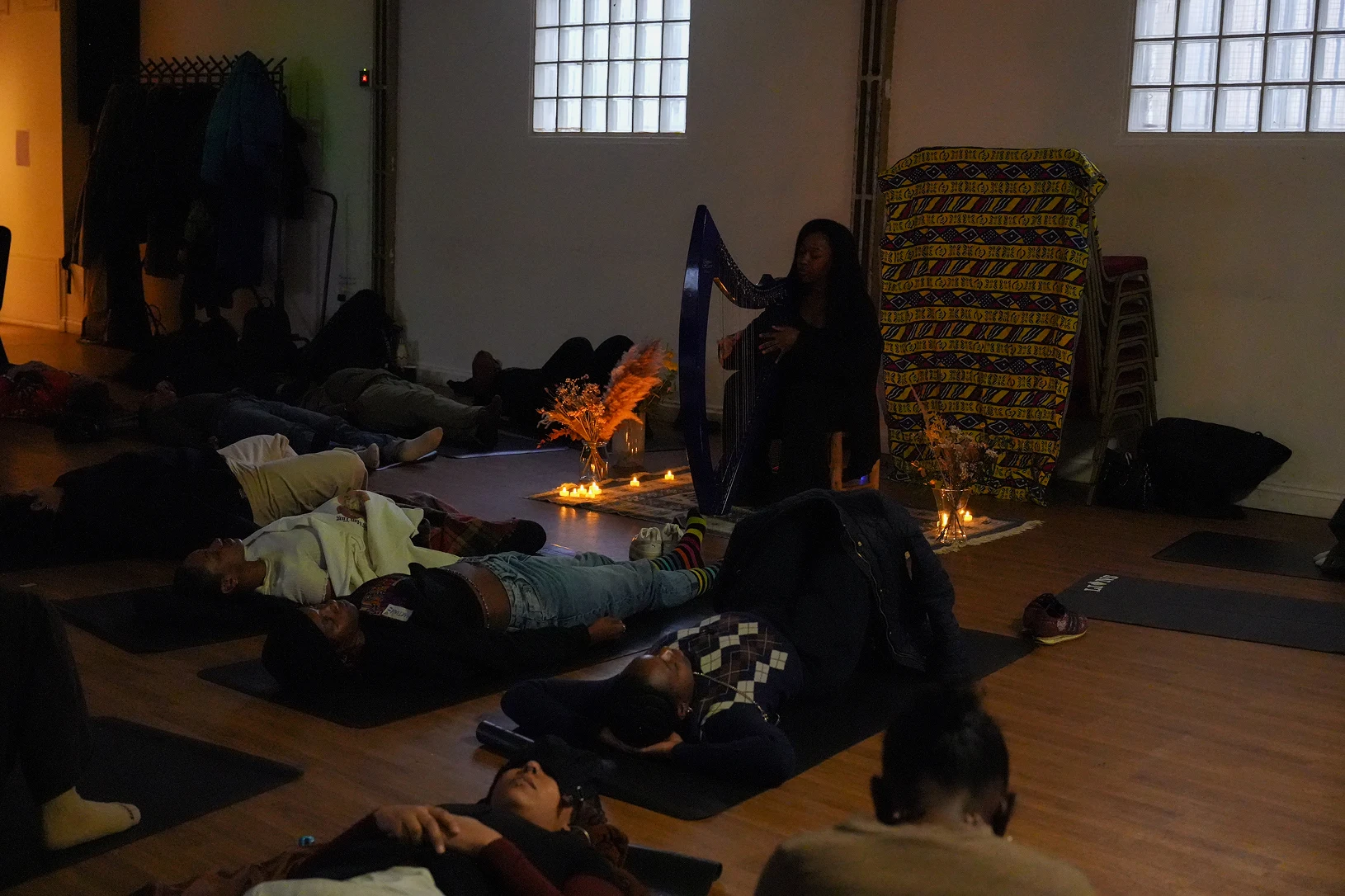 Experiments in cosmic dreams 1 People lying down on yoga mats in a dimly candle-lit room while someone plays the harp