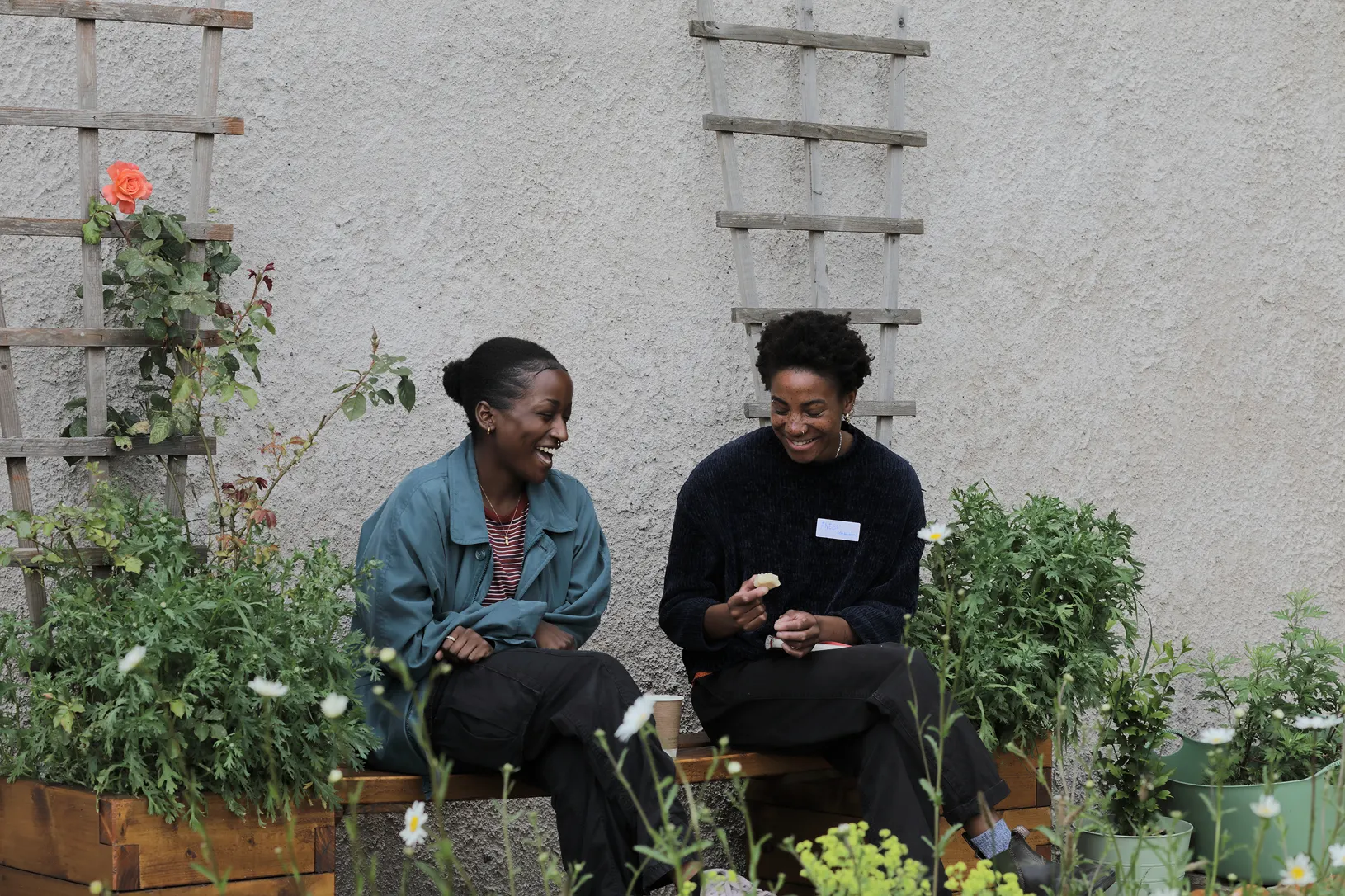 Healing in Community 2 Two people sitting among planters full of thriving plants, laughing