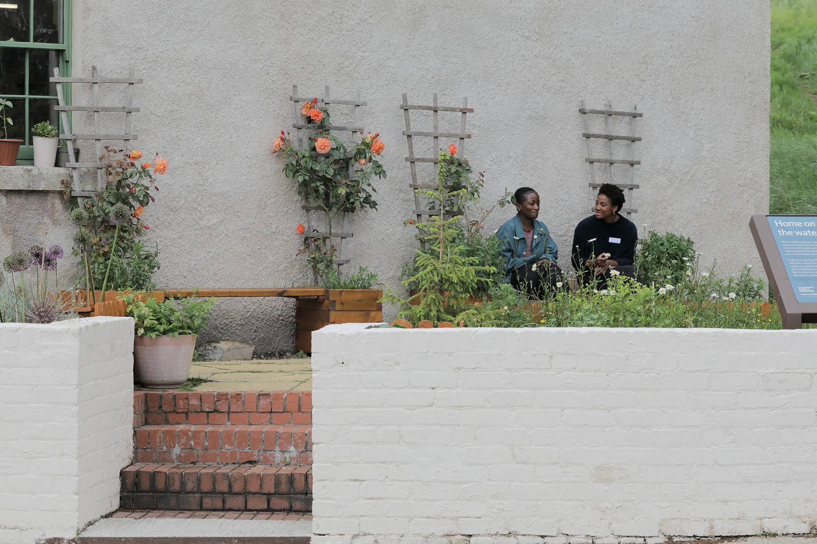 Healing in Community 4 Two people sitting among planters full of thriving plants, having a conversation